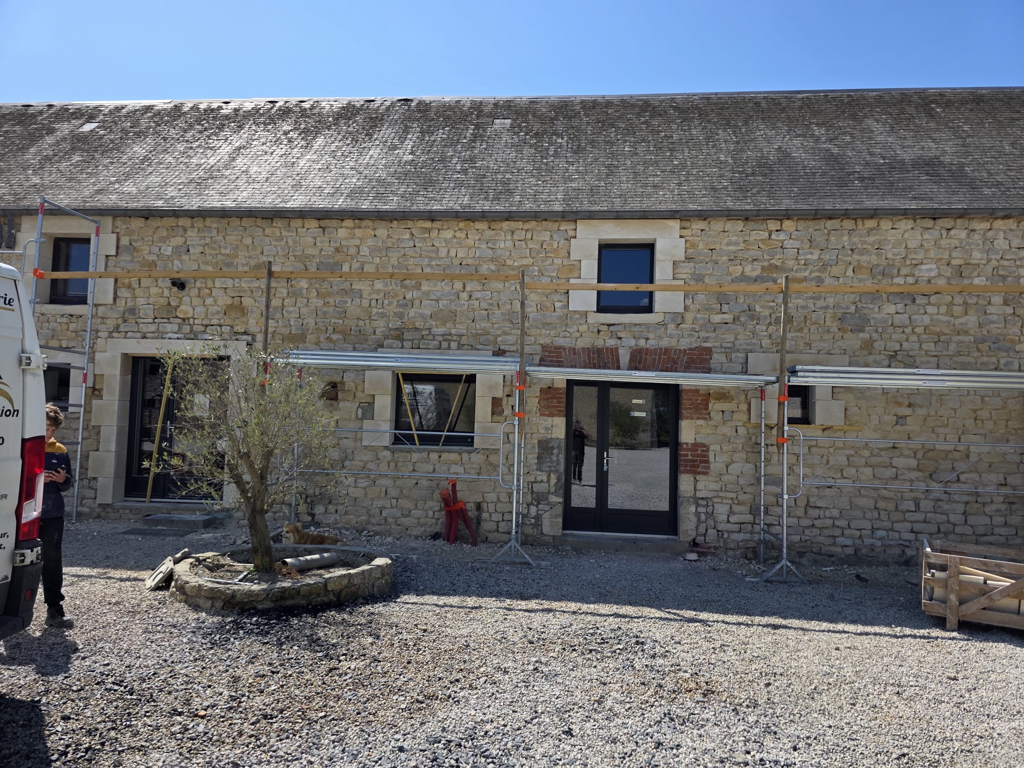 Façade en pierre d'une maison en rénovation avec échafaudage et portes vitrées noires