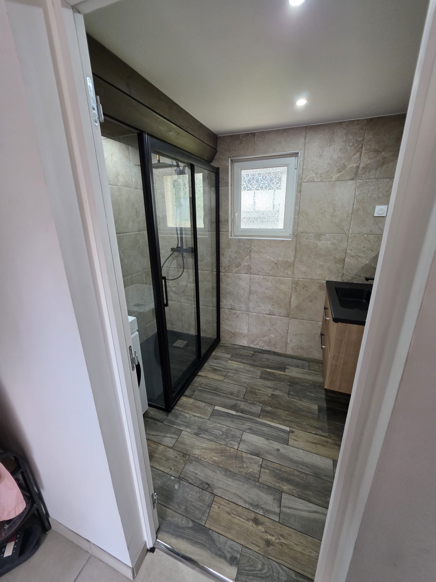 Salle de bain rénovée avec carrelage effet bois et douche vitrée noire - LR Rénovation