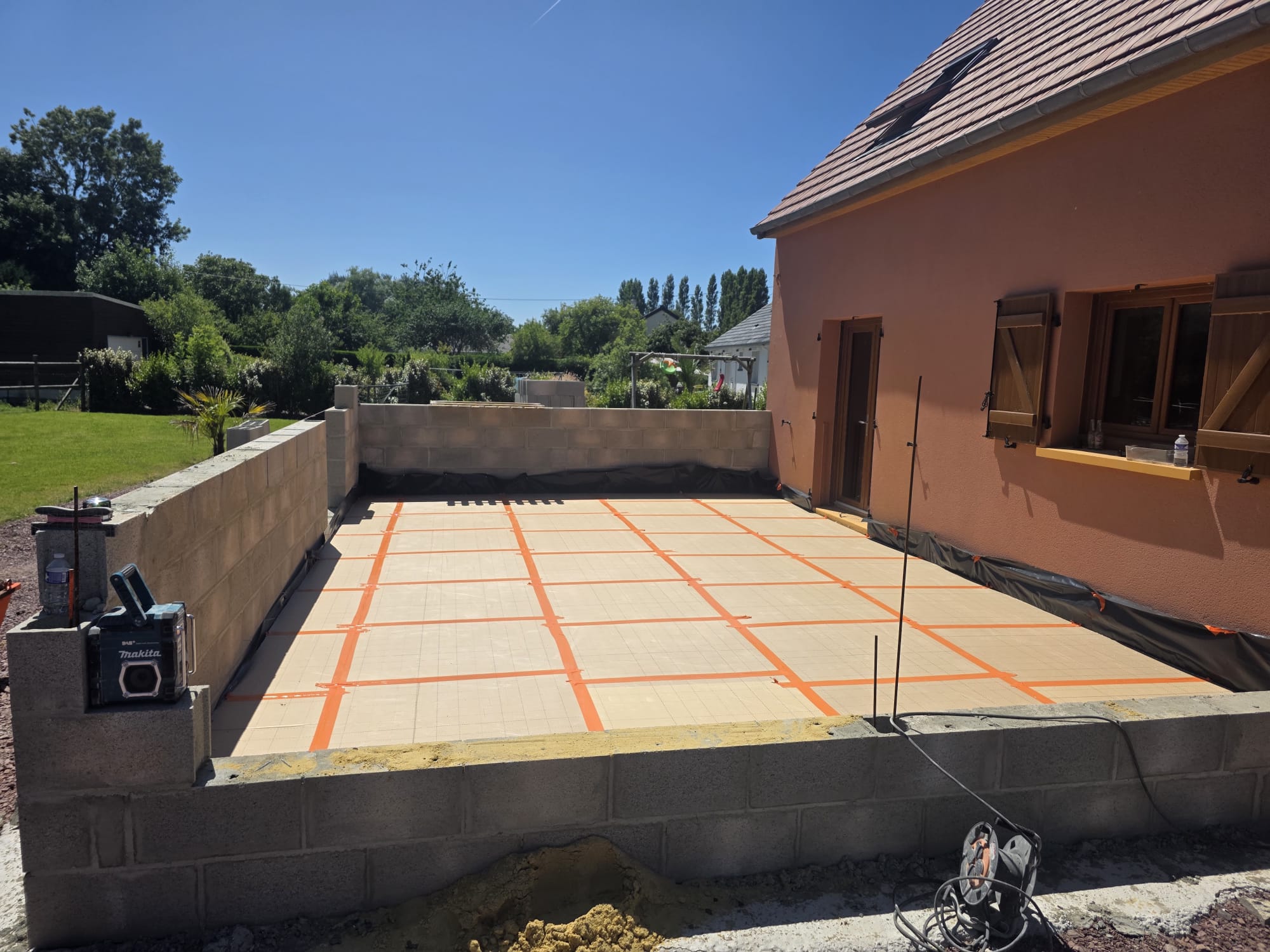 Terrasse en construction avec mur en parpaings et maison volets bois - LR Rénovation